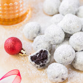 rum ball with a bite in front of pile of rum balls coated in confectioners' sugar.