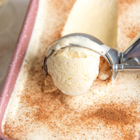 ice cream scoop pulling forward a scoop of eggnog ice cream sprinkled with nutmeg.