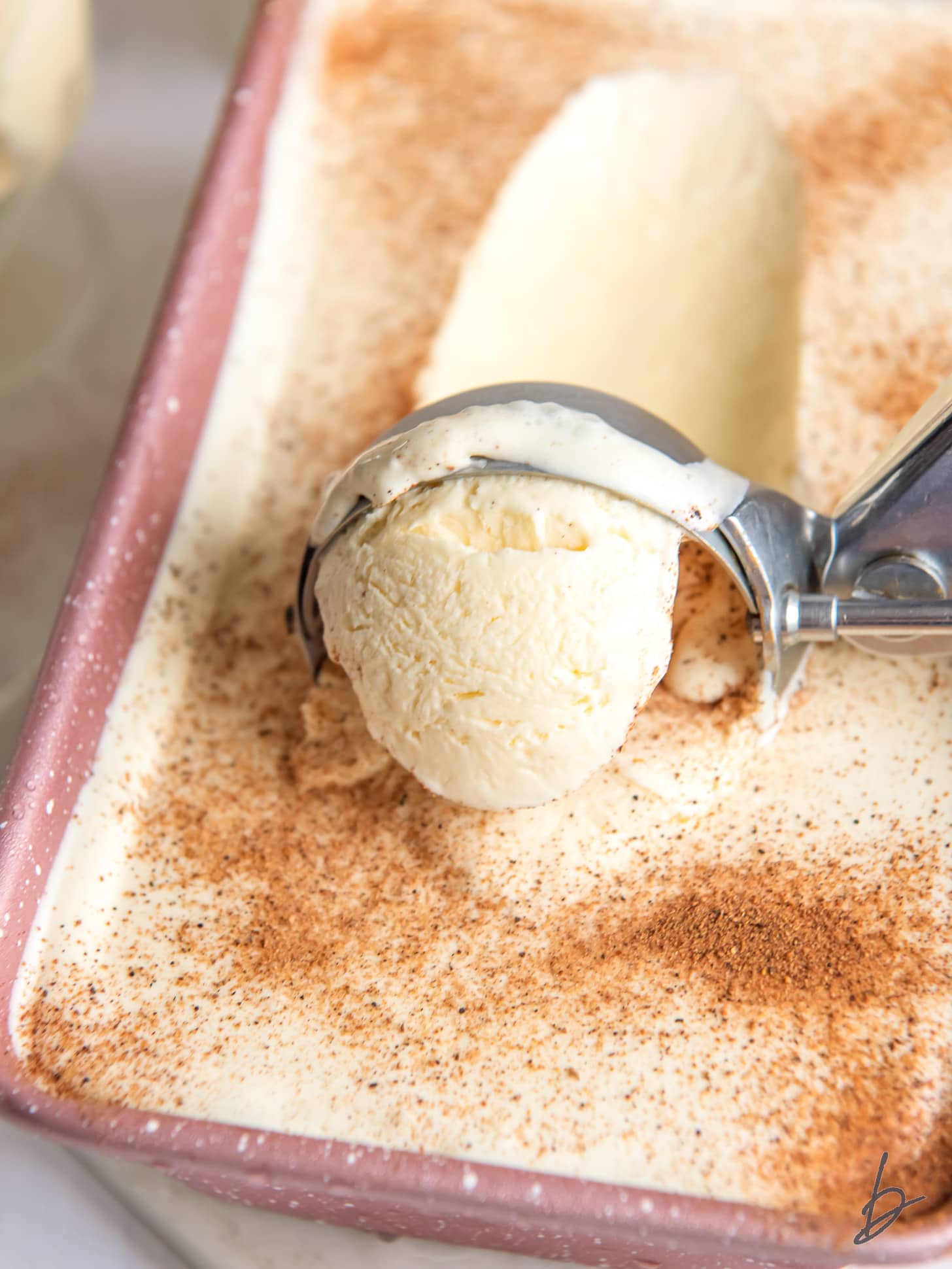 ice cream scoop pulling forward a scoop of eggnog ice cream sprinkled with nutmeg.