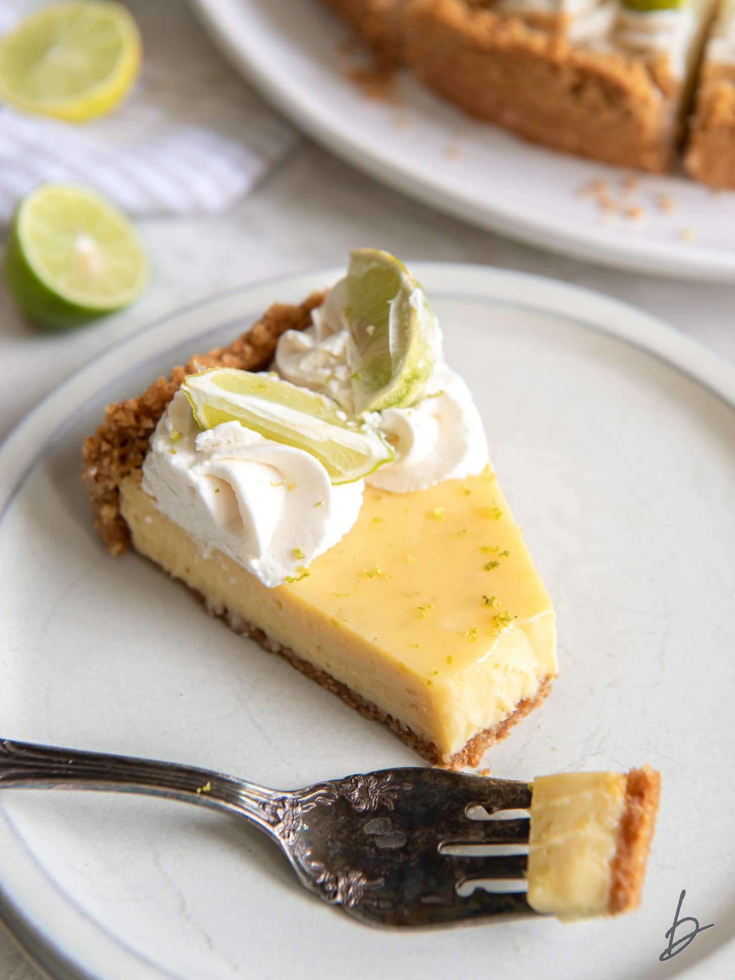 fork holding a bite of key lime pie on white round plate.