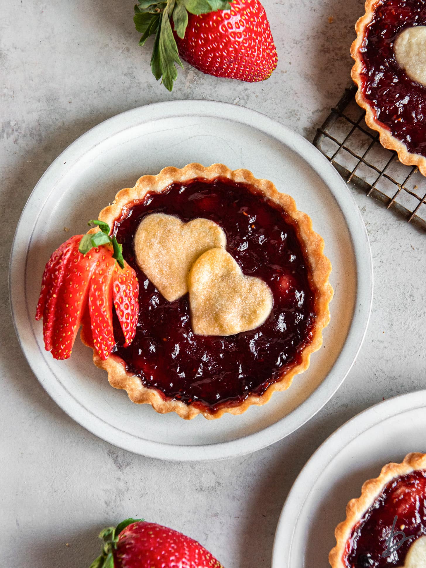 strawberry jam tart with shortbread crust and two heart cut outs on top and fresh strawberry for garnish.
