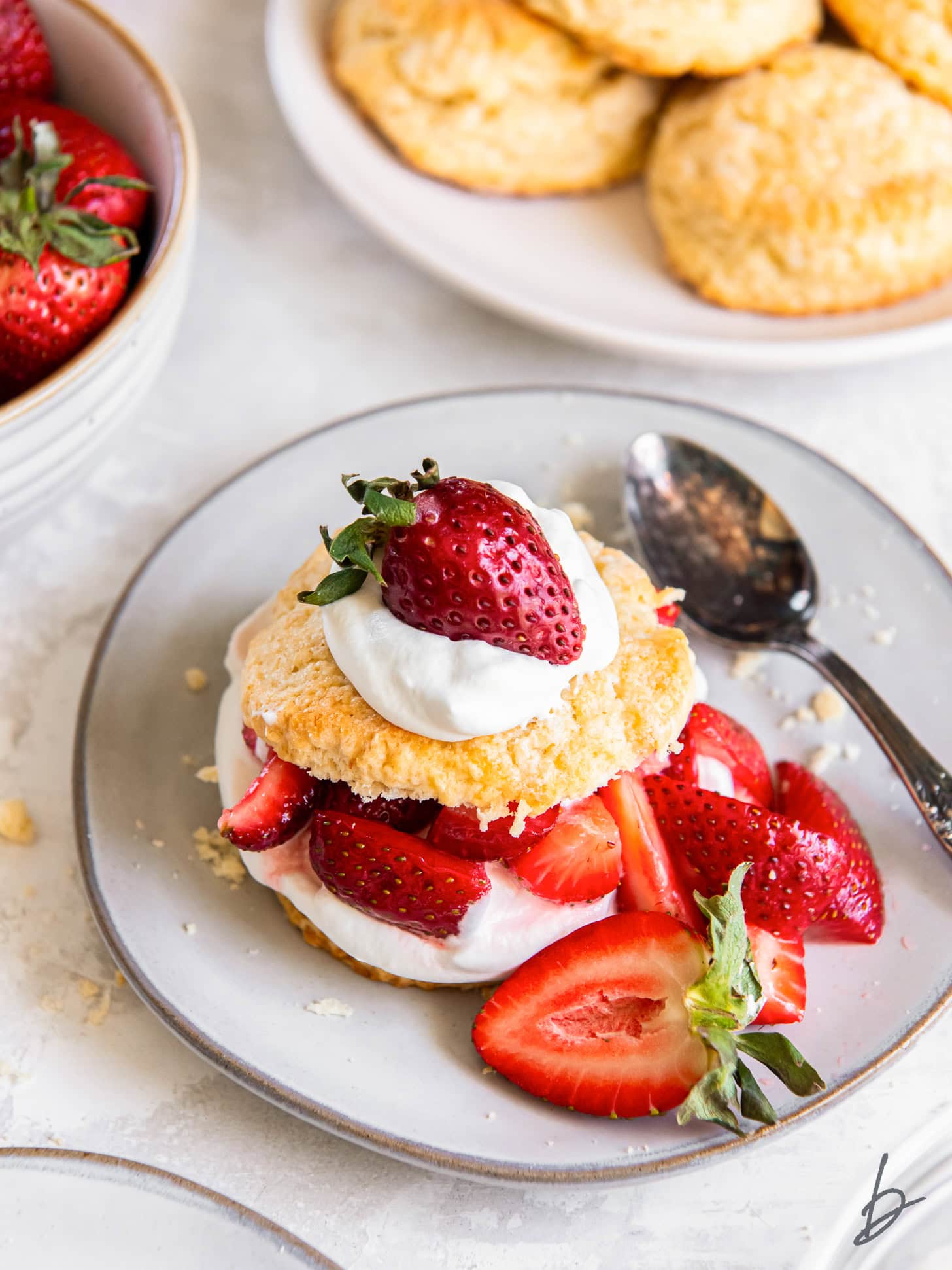strawberry shortcake on a plate with extra strawberries and spoon.
