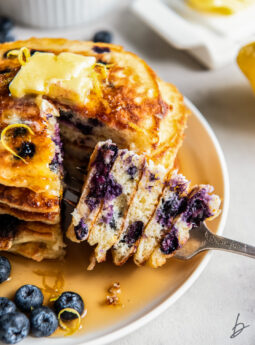 fork holding bite from stack of fluffy lemon blueberry pancakes.