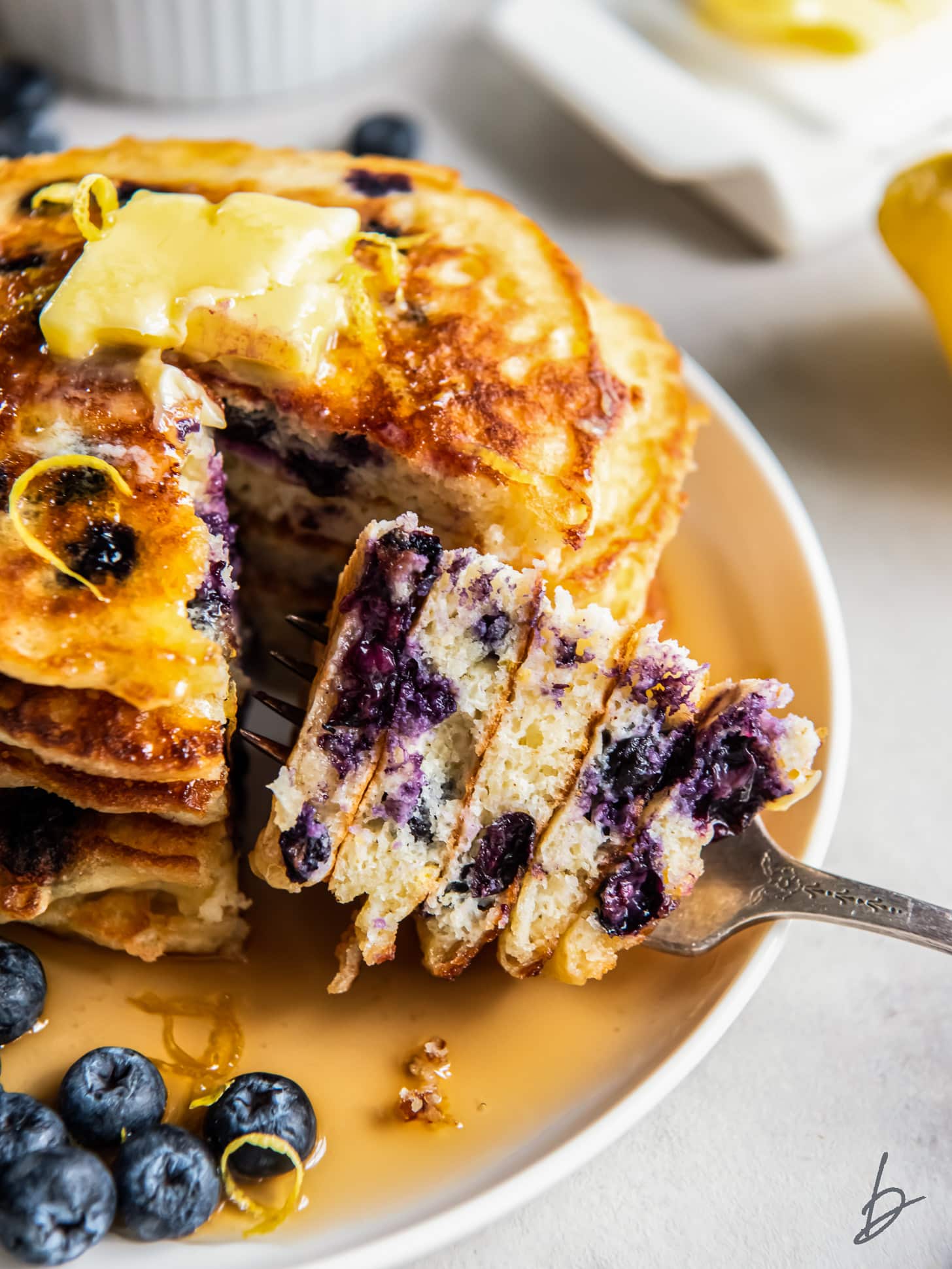 fork holding bite from stack of fluffy lemon blueberry pancakes.