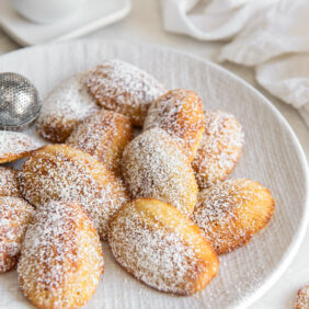 madeleines on a plate with a dusting of confectioners' sugar.