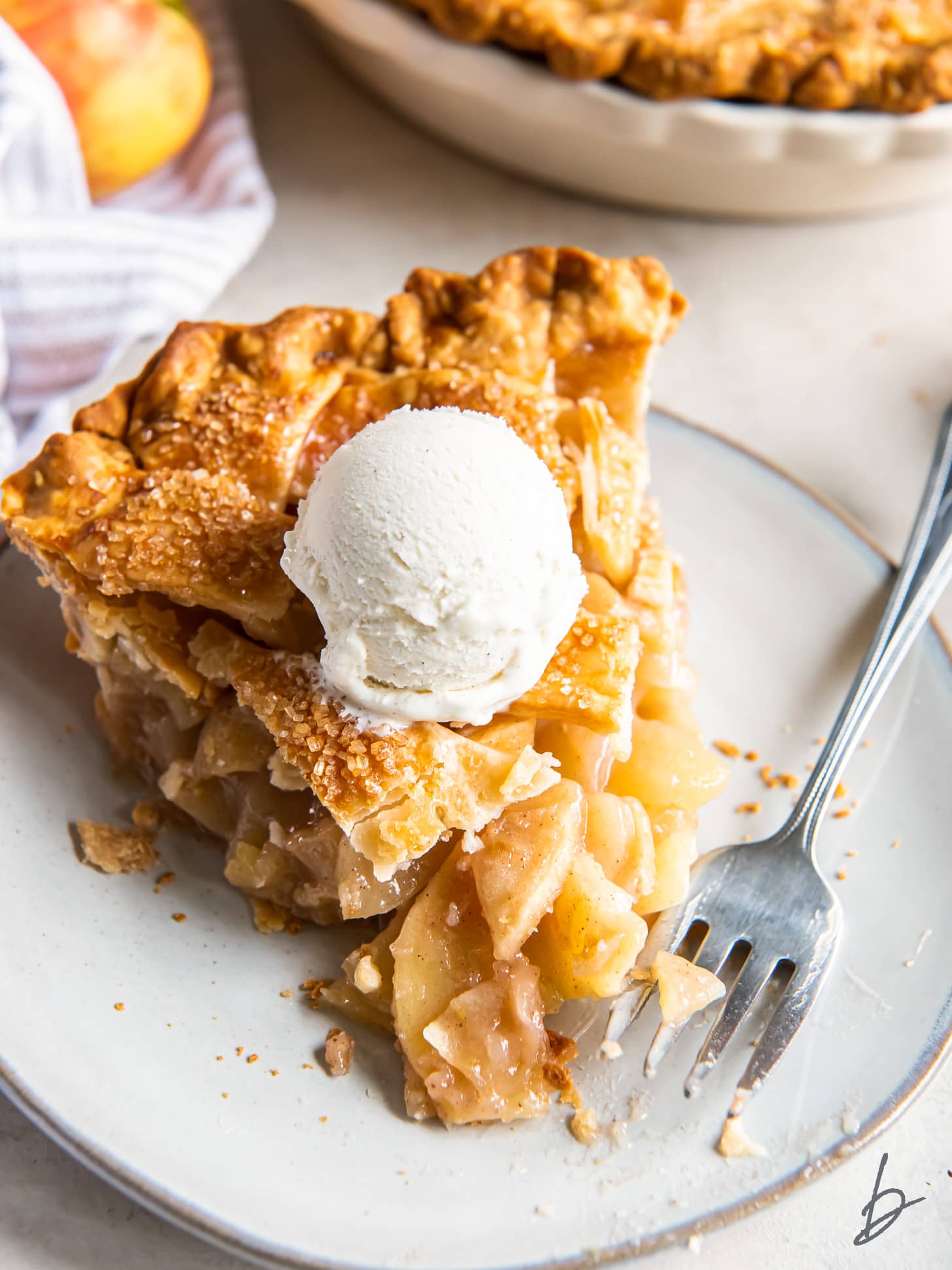 slice of apple pie with scoop of vanilla ice cream and a fork taking a bite from the corner.