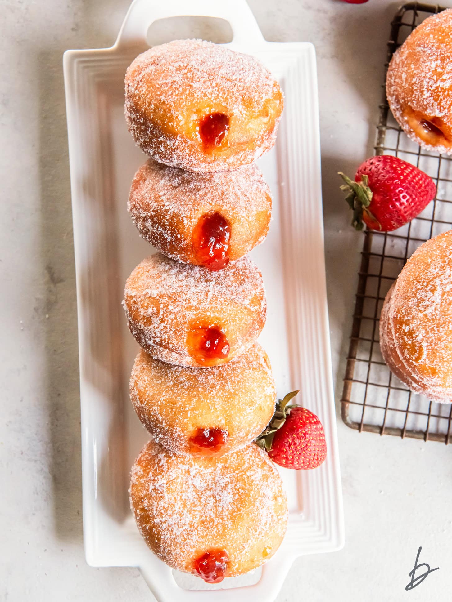 jelly donuts leaning on each other on a long rectangle serving plate.