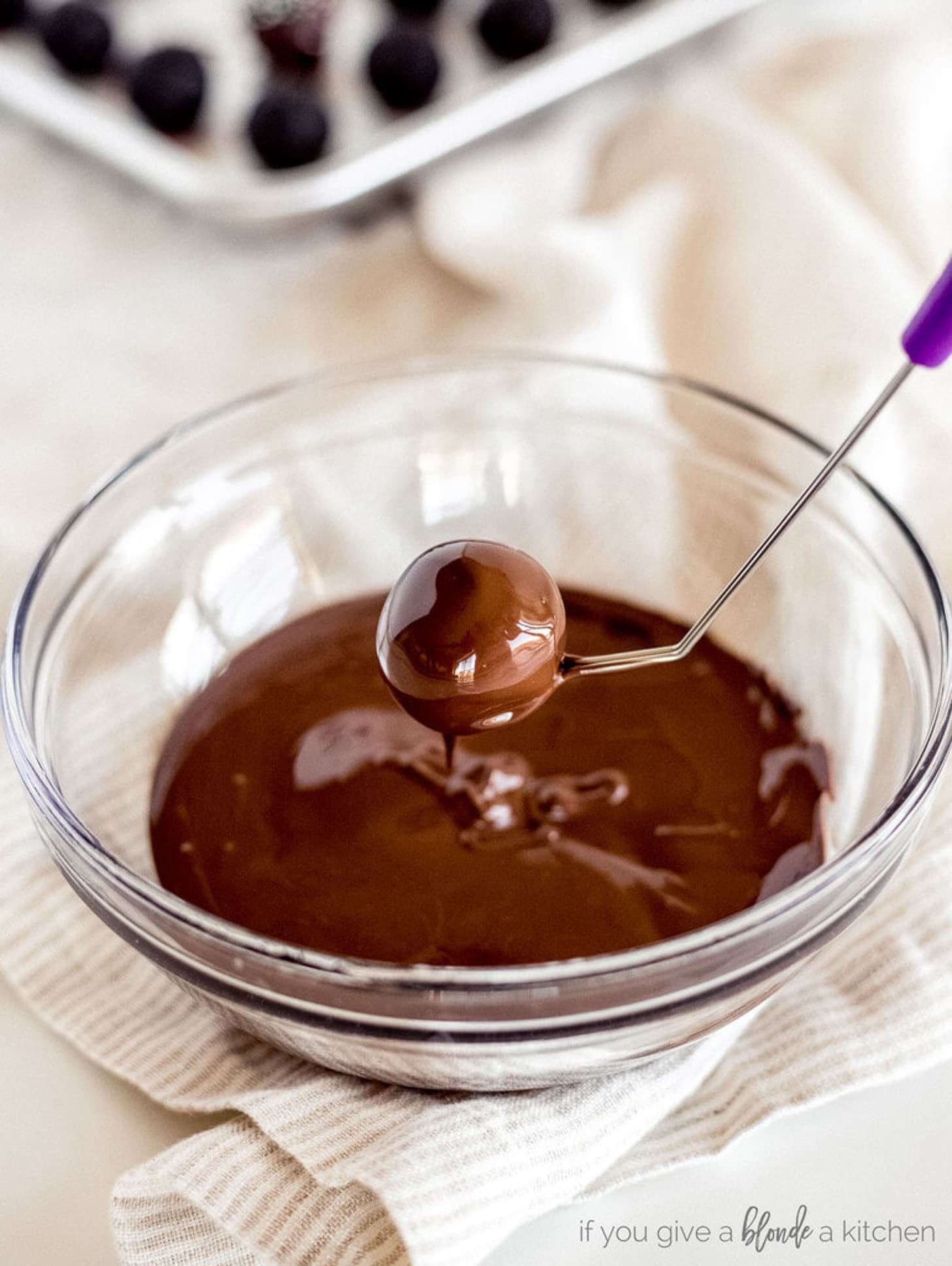 dipping tool holding chocolate covered oreo truffle over bowl of melted chocolate.