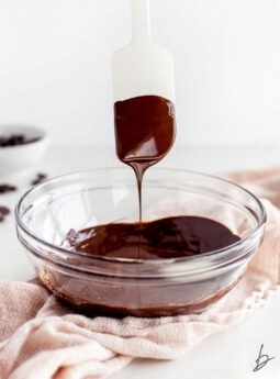 silicone spatula with melted chocolate dripping into bowl of melted chocolate.