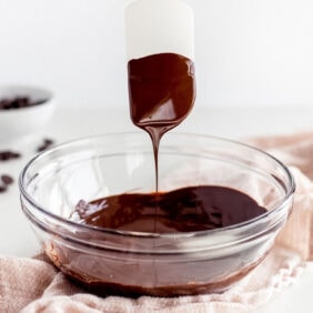 silicone spatula with melted chocolate dripping into bowl of melted chocolate.