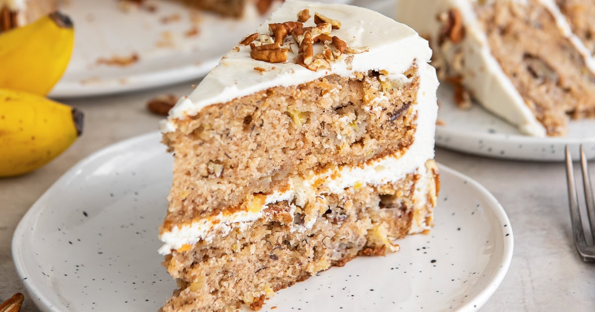 two layer slice of cake with frosting in middle and on top and topped with pecans.