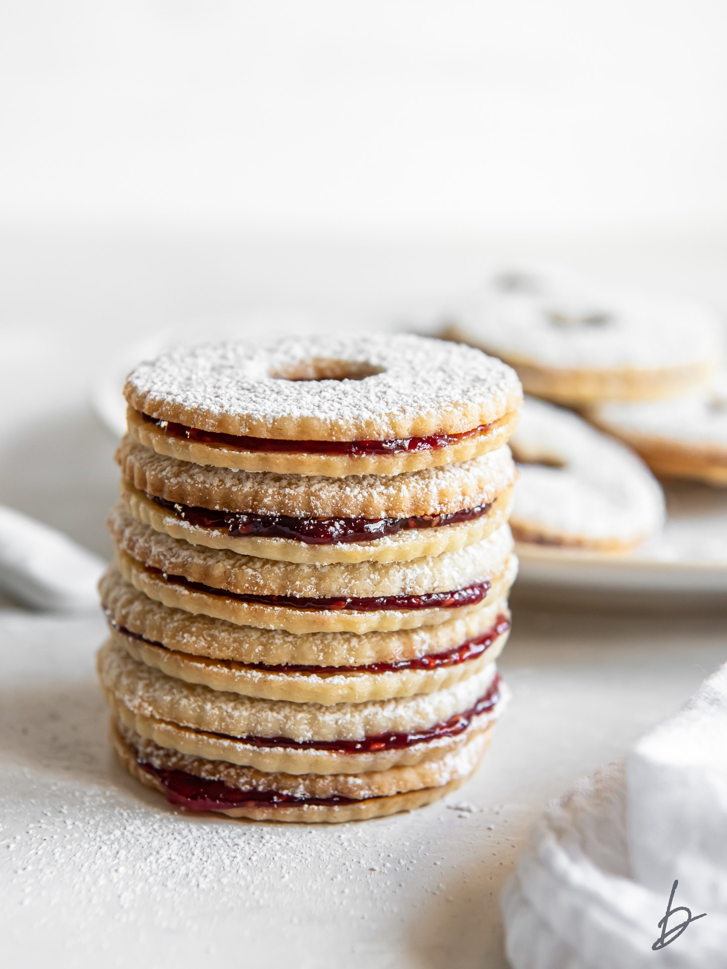 stack of jam sandwich cookies in front of plate.