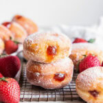two jelly filled donuts stacked on top of each other with fresh strawberries next to them.