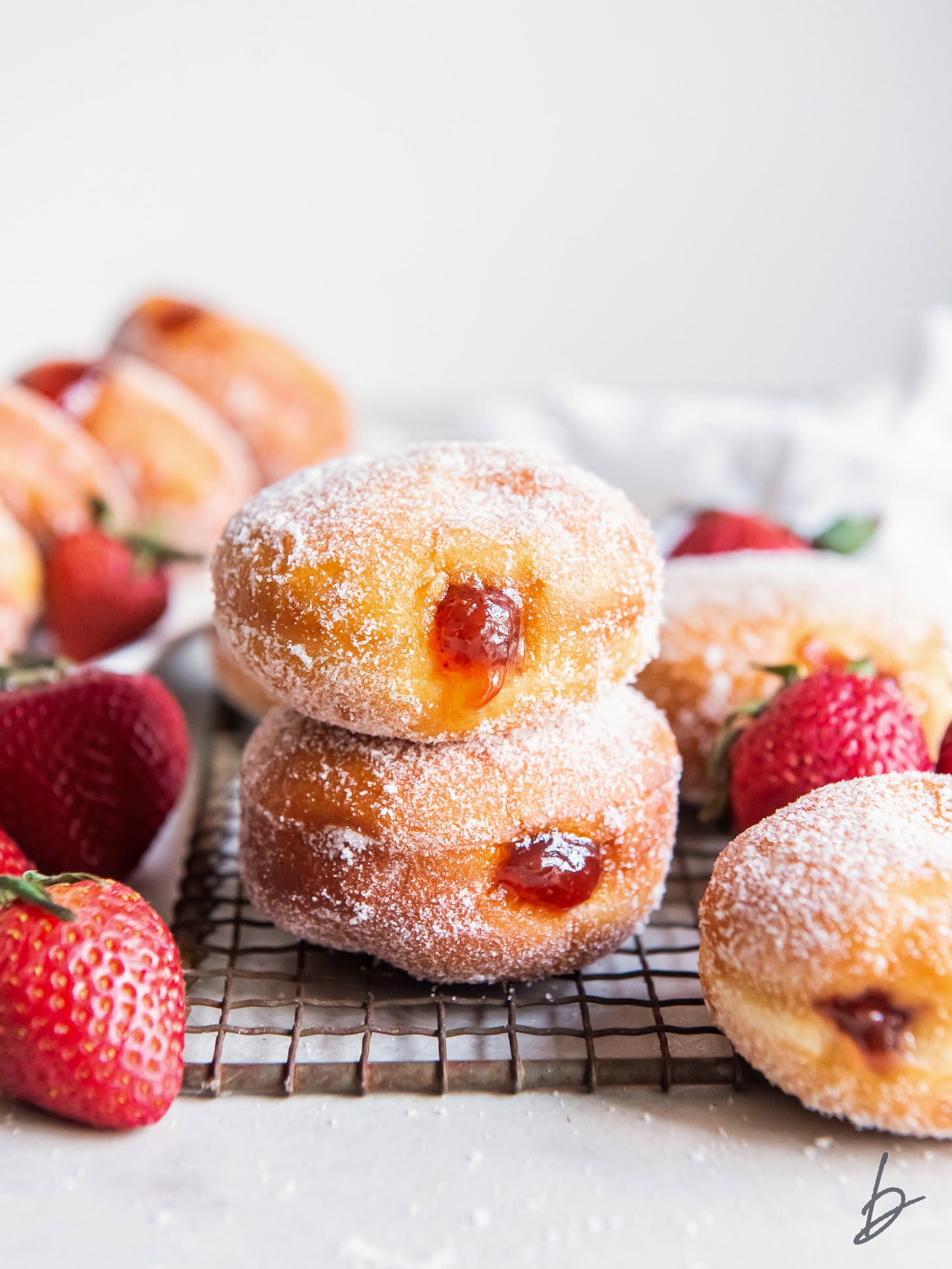 two jelly filled donuts stack o top of each other with fresh strawberries next to them
