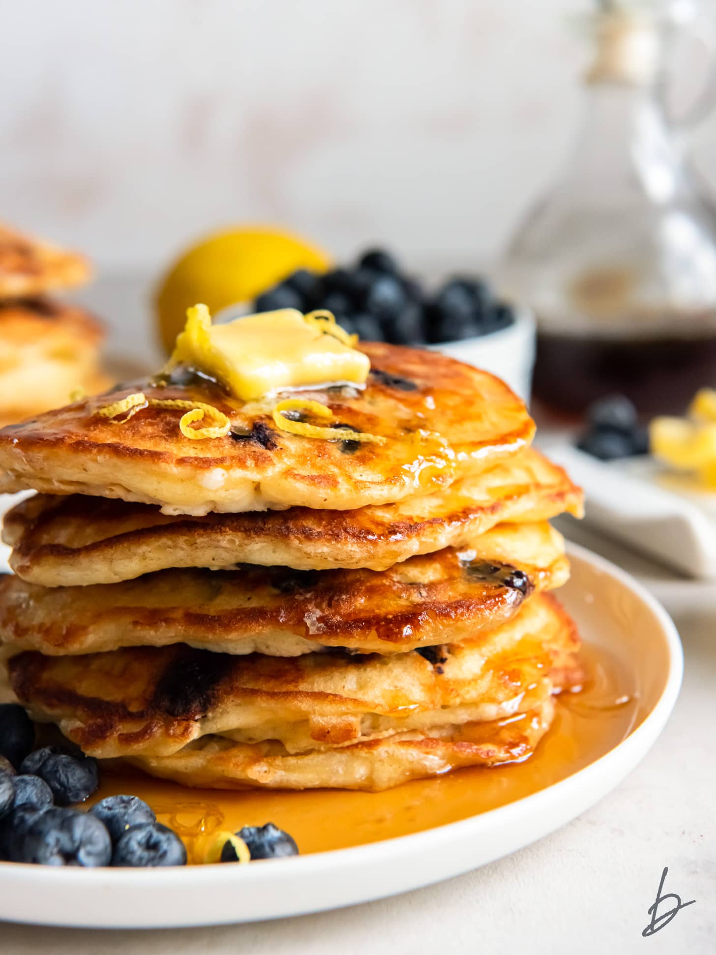 stack of lemon blueberry pancakes with pat of butter and maple syrup on top.
