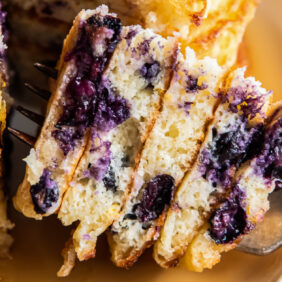 fork holding stacked bite of lemon blueberry pancakes.