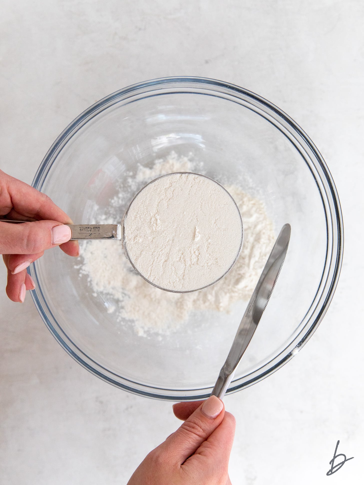 hand holding cup full of flour with knife next to it.