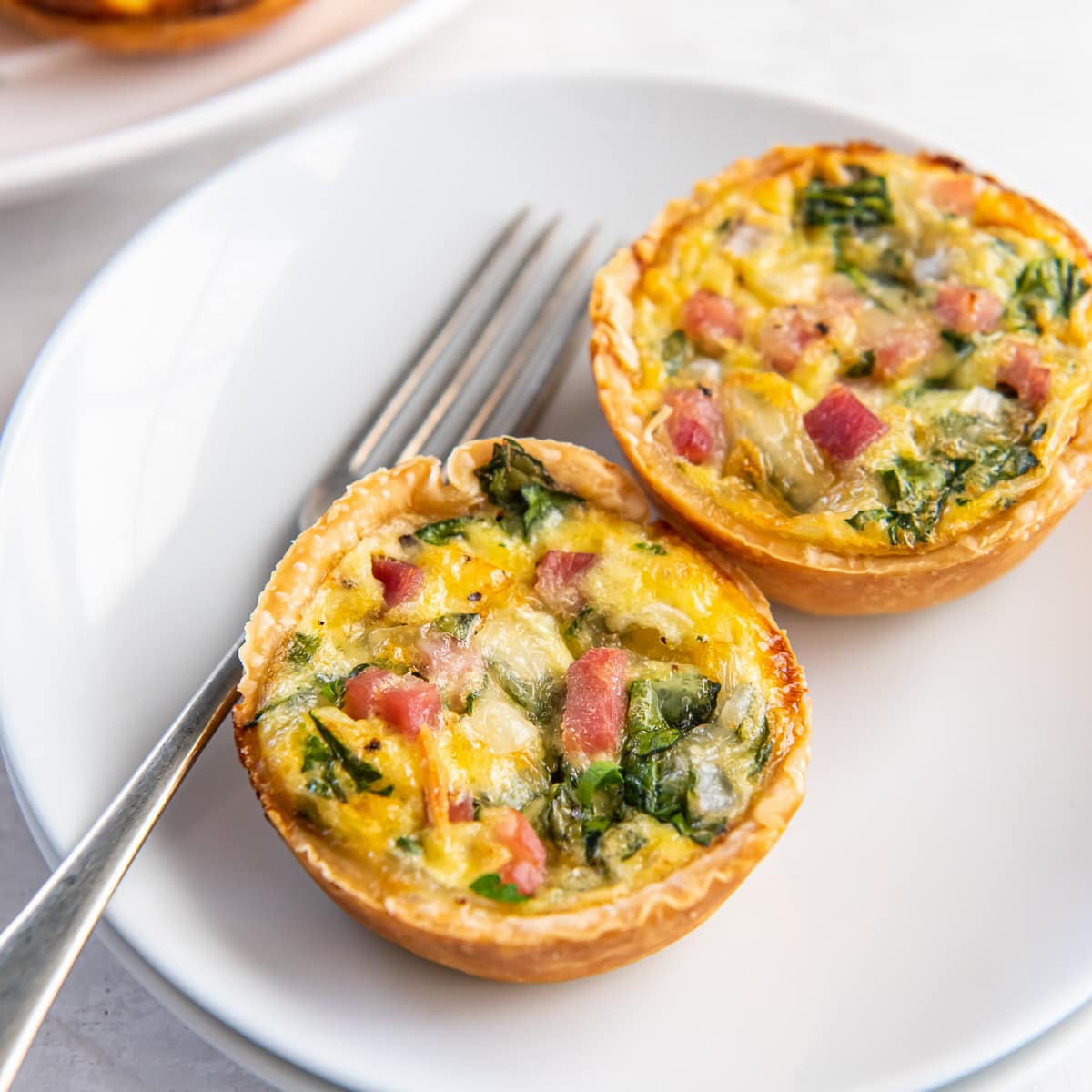 two mini quiches on a white plate with a fork.