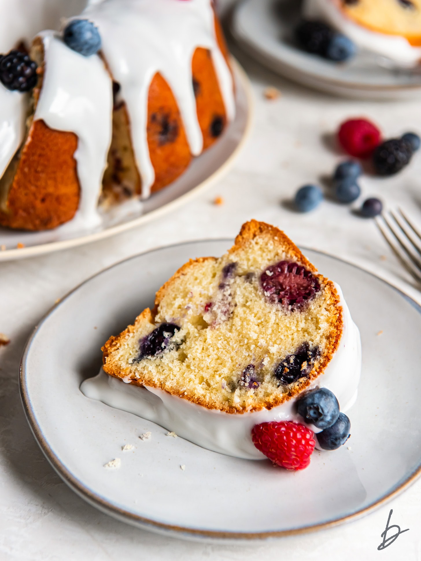 slice of mixed berry bundt cake on a plate with a raspberry and blueberry garnish.