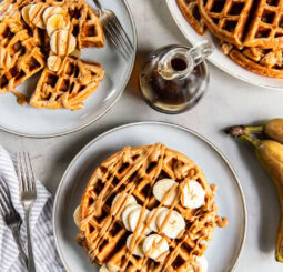 tabletop with plates of peanut butter banana waffles garnished with fresh banana slices and peanut butter.