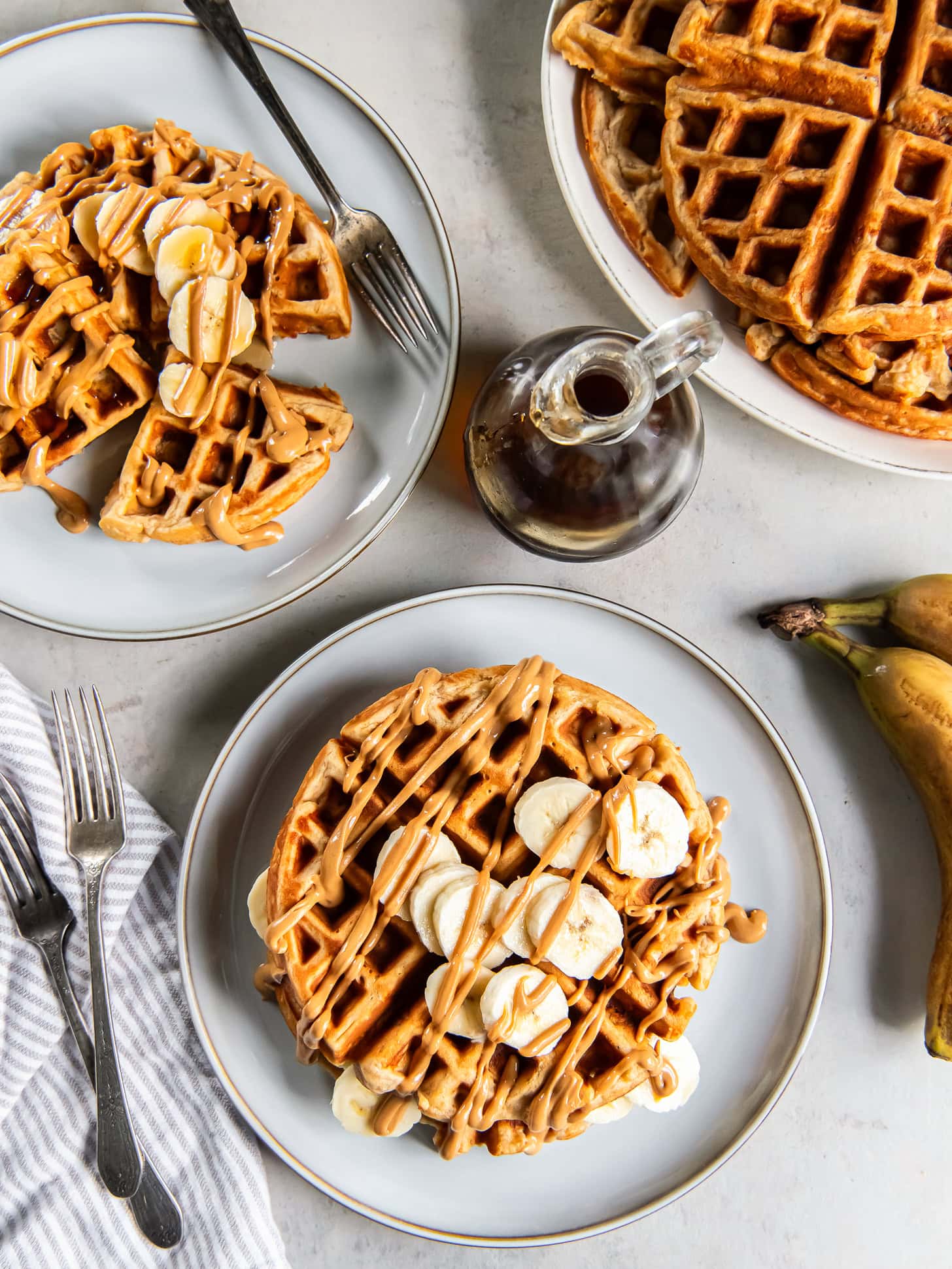 Tabletop with plates of peanut butter banana waffles garnished with fresh banana slices and peanut butter.