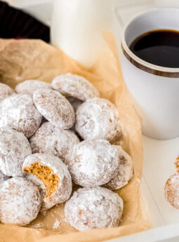 pfeffernusse cookie with bite on pile of cookies with powdered sugar next to mug of coffee.