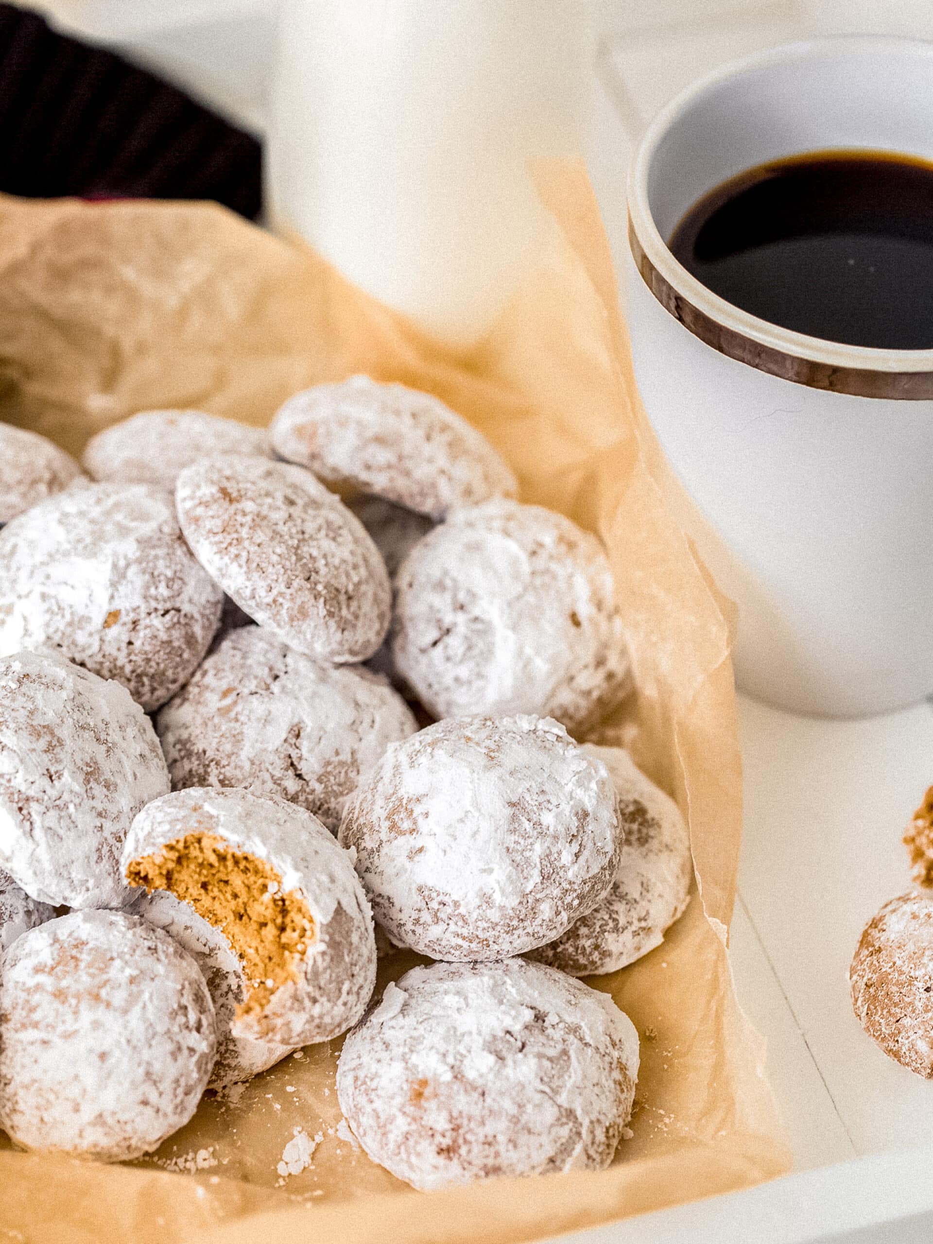 pfeffernusse cookie with bite on pile of cookies with powdered sugar next to mug of coffee.