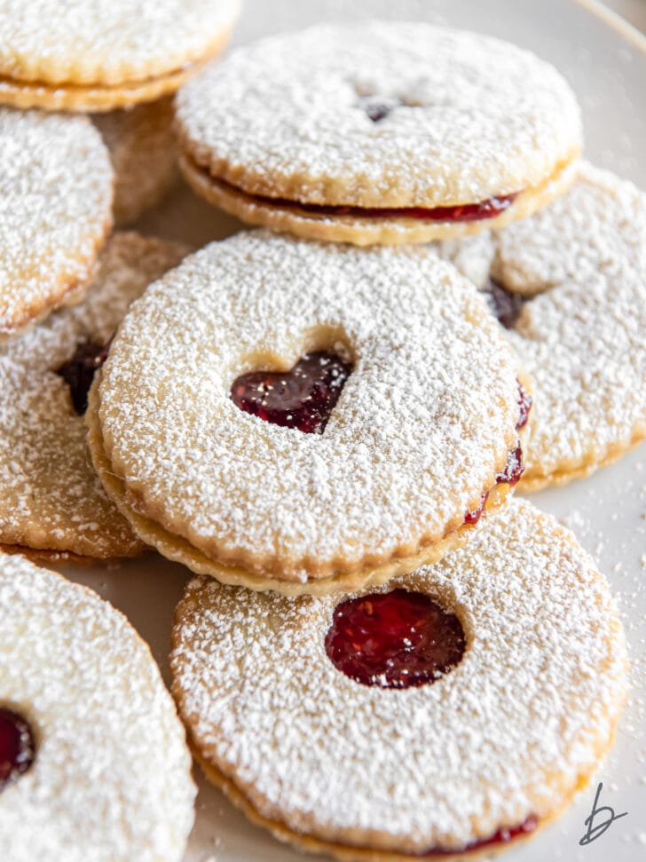 jam sandwich cookies dusted in confectioners' sugar on a plate.