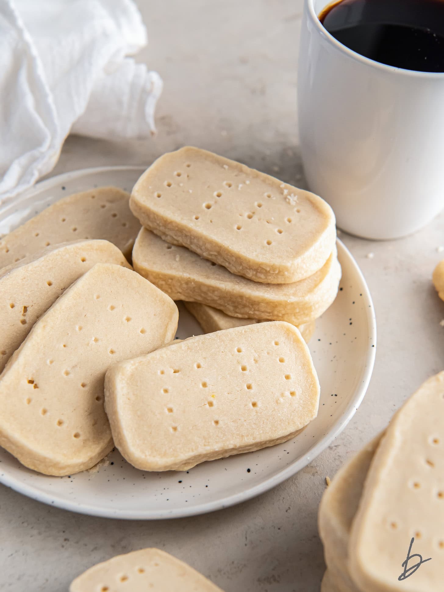 scottish shortbread cookies on white round plate next to mug of coffee.