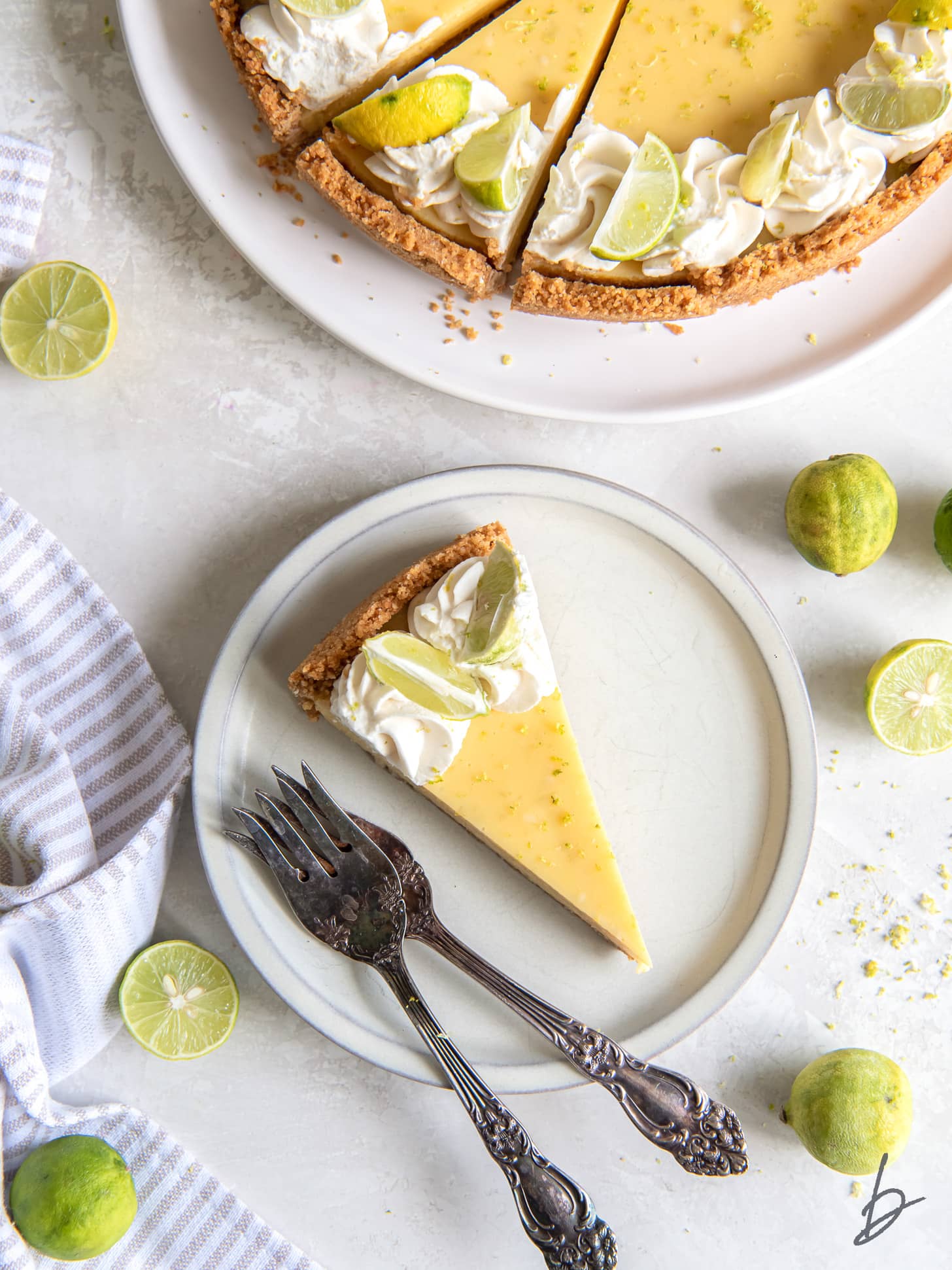 key lime pie slice on plate with two forks next to some limes.