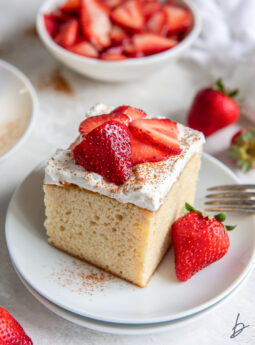 square slice of tres leches cake on a plate with whipped cream topping and strawberries.