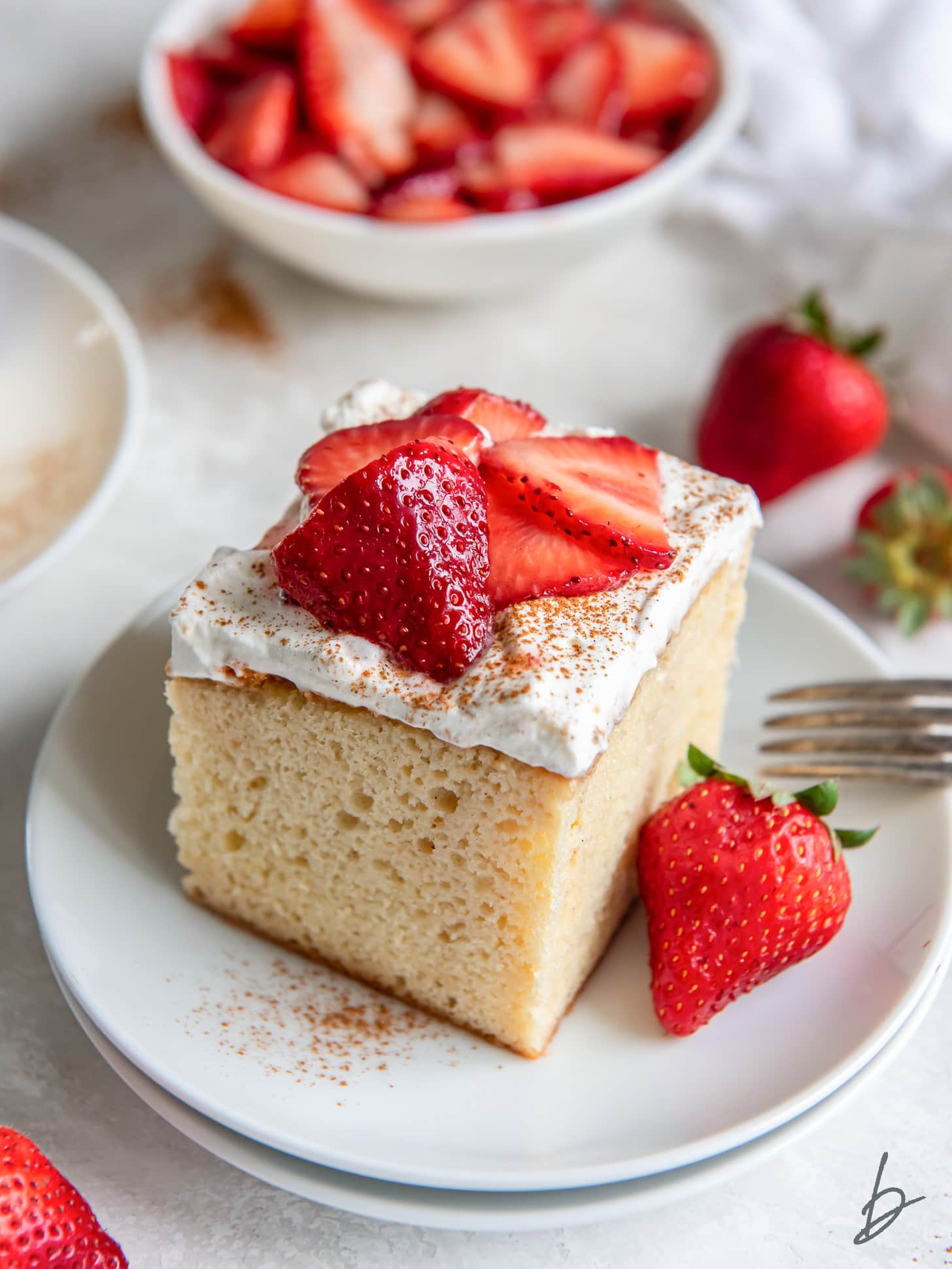 square slice of tres leches cake on a plate with whipped cream topping and strawberries.