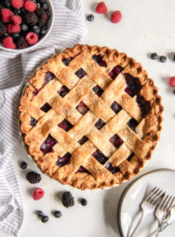 triple berry pie on tabletop with a bowl of fresh berries.