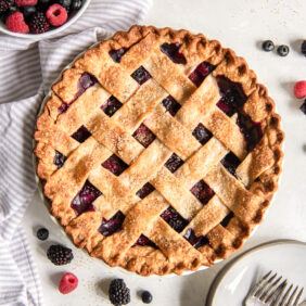 triple berry pie on tabletop with a bowl of fresh berries.