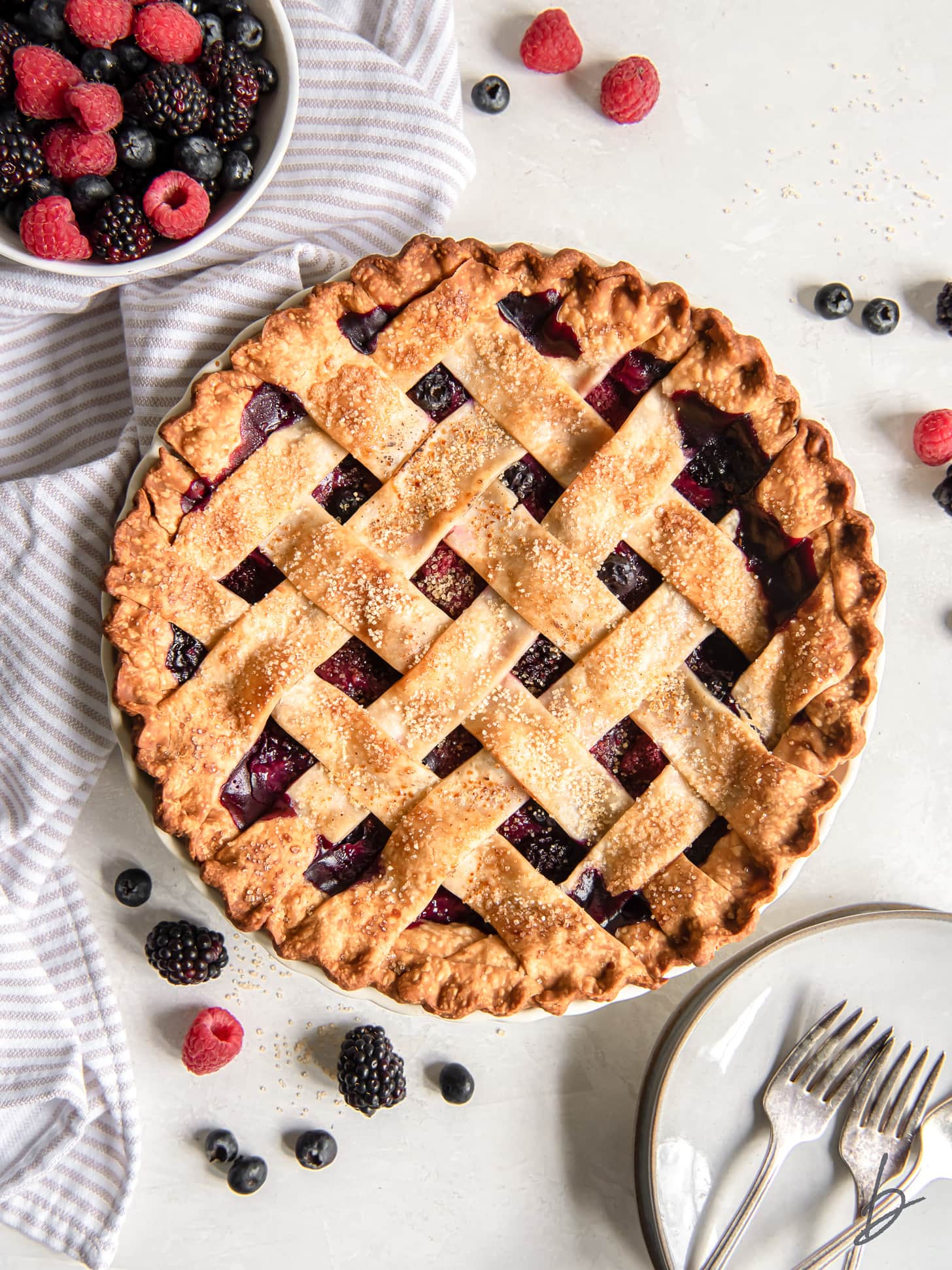 triple berry pie on tabletop with a bowl of fresh berries.
