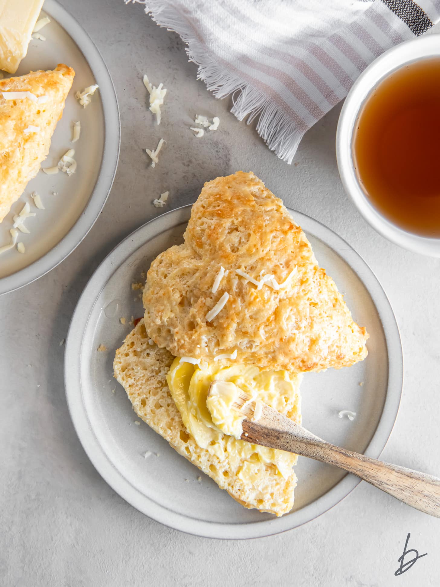 butter spread on bottom half of a cheese scone on a plate.