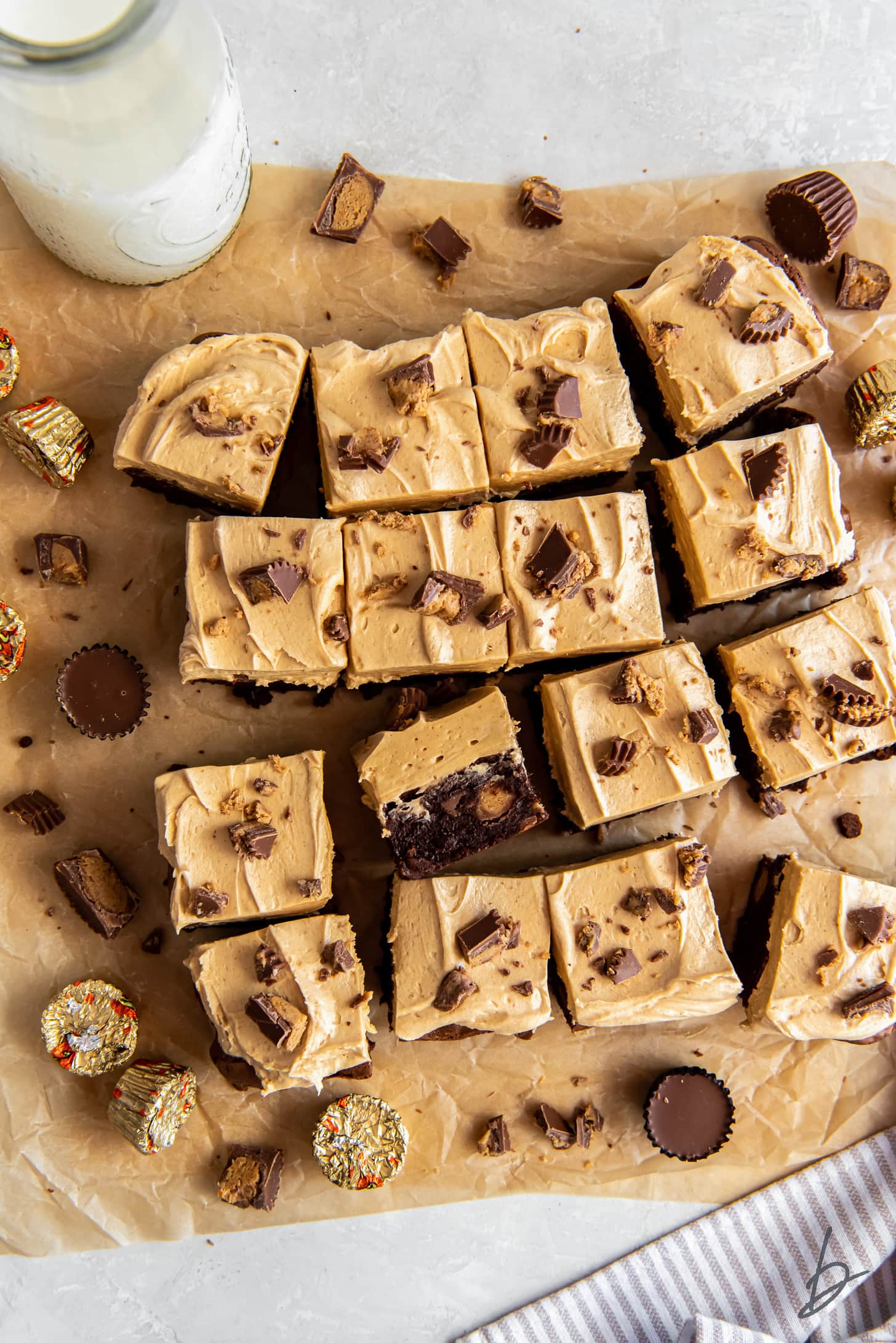 peanut butter brownies with frosting and peanut butter cups on parchment paper.