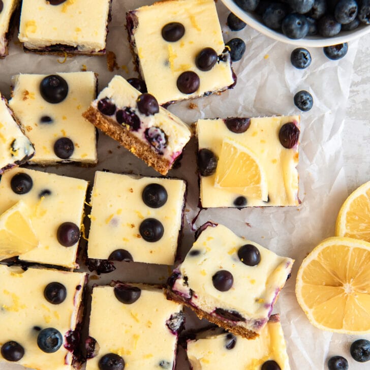 lemon blueberry cheesecake bars on wax paper with blueberries.