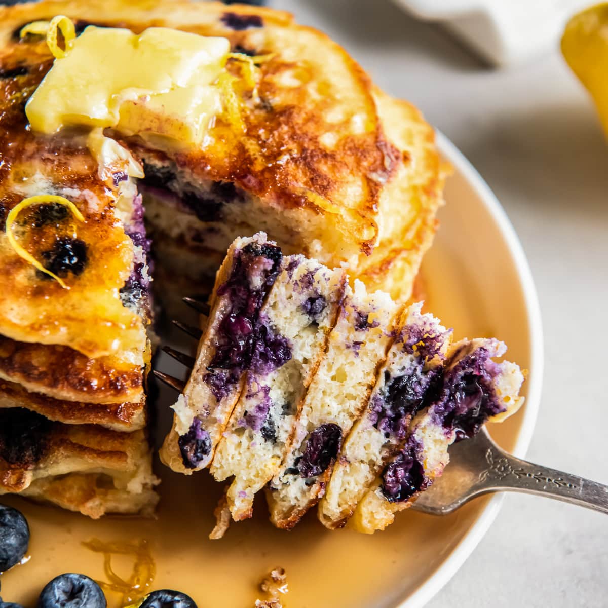 fork holding stacked bite of lemon blueberry pancakes.