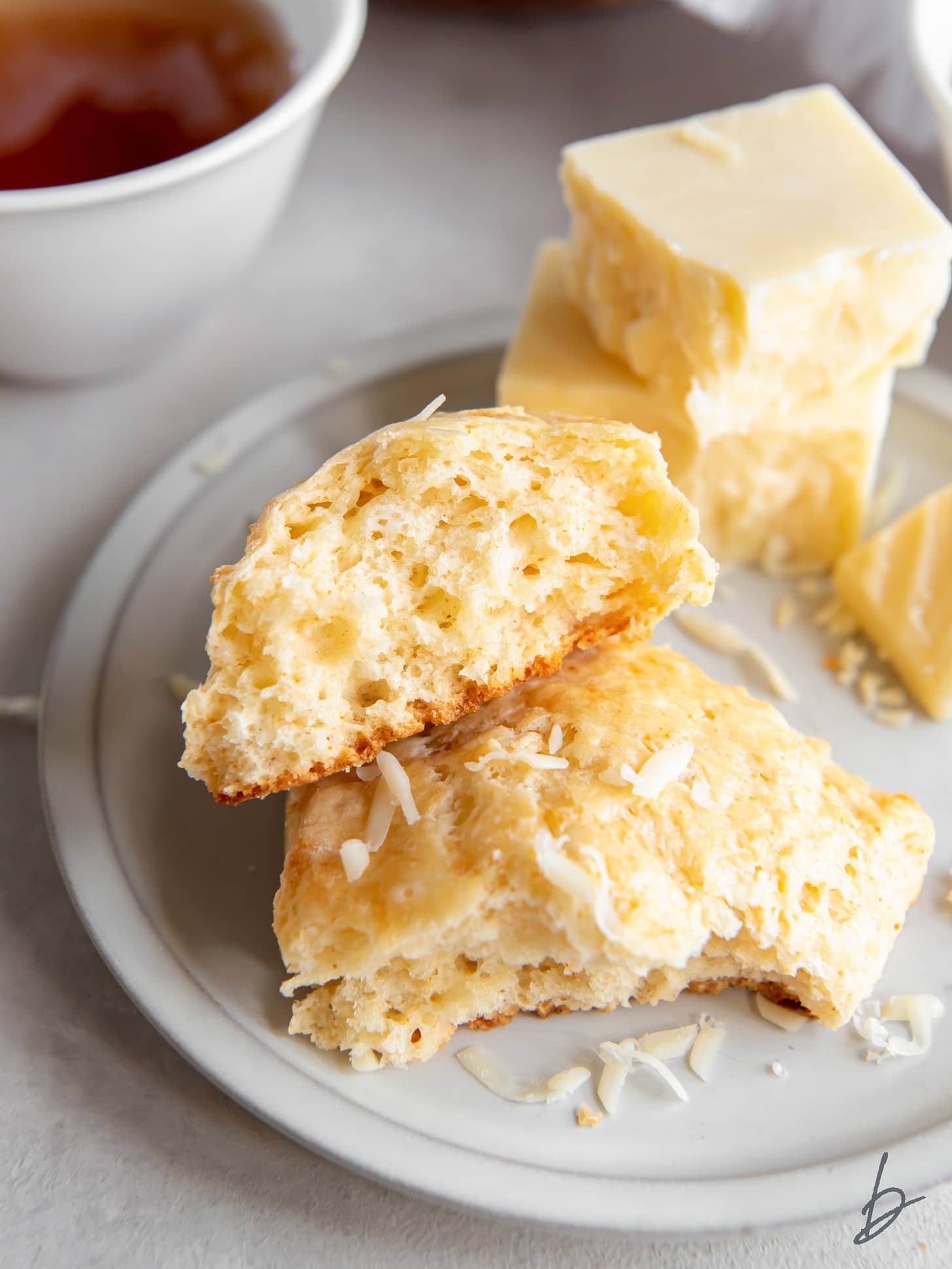 two halves of a fluffy cheese scone on a plate with a couple small squares of sharp cheddar cheese.