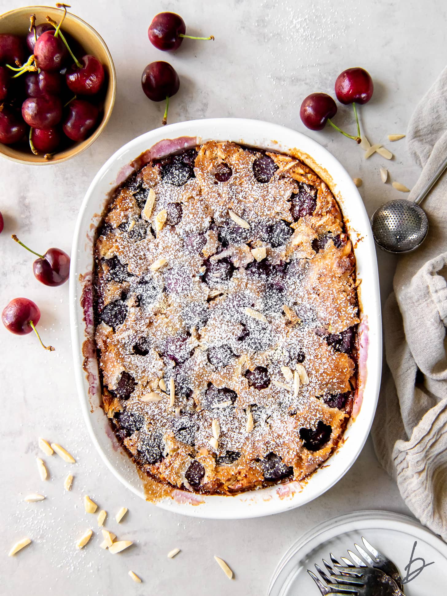 baking dish of cherry clafoutis next to bowl of fresh cherries.