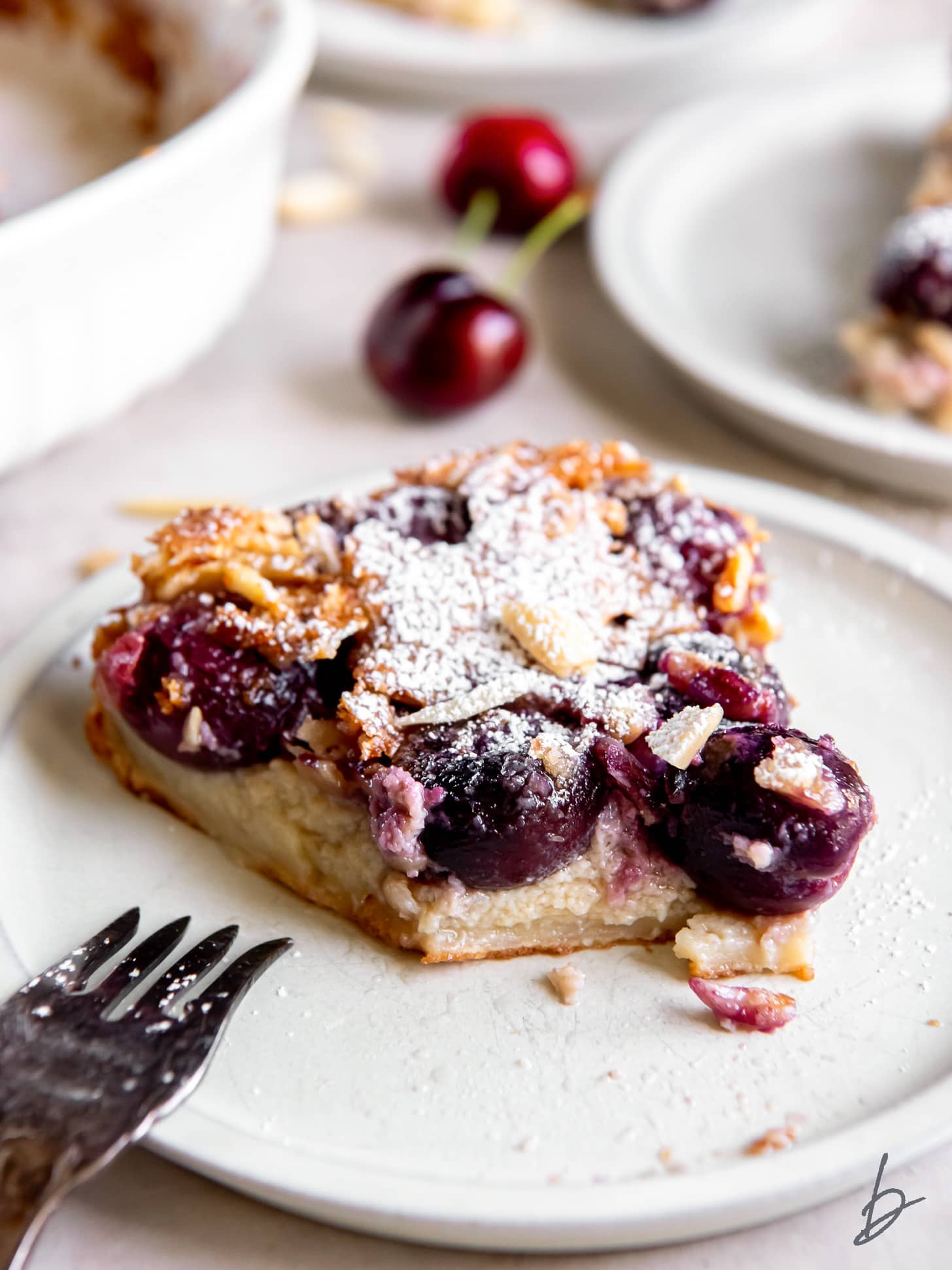 plate with a slice of cherry clafoutis with a bite taken to show juicy cherries inside.