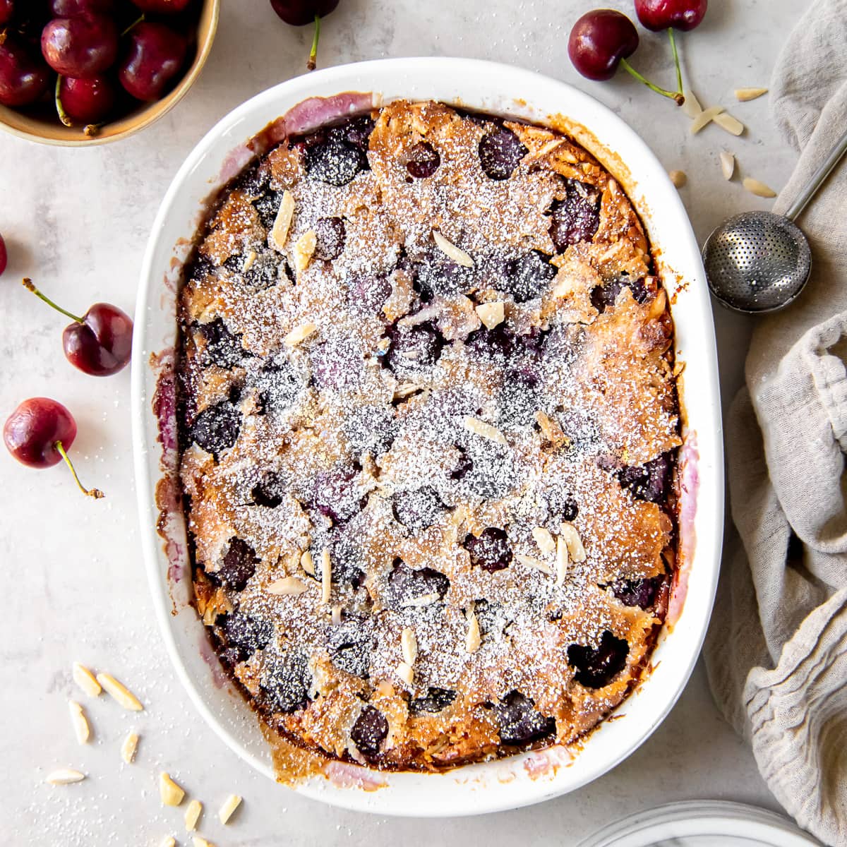 cherry clafoutis dusted with confectioners' sugar in a baking dish.
