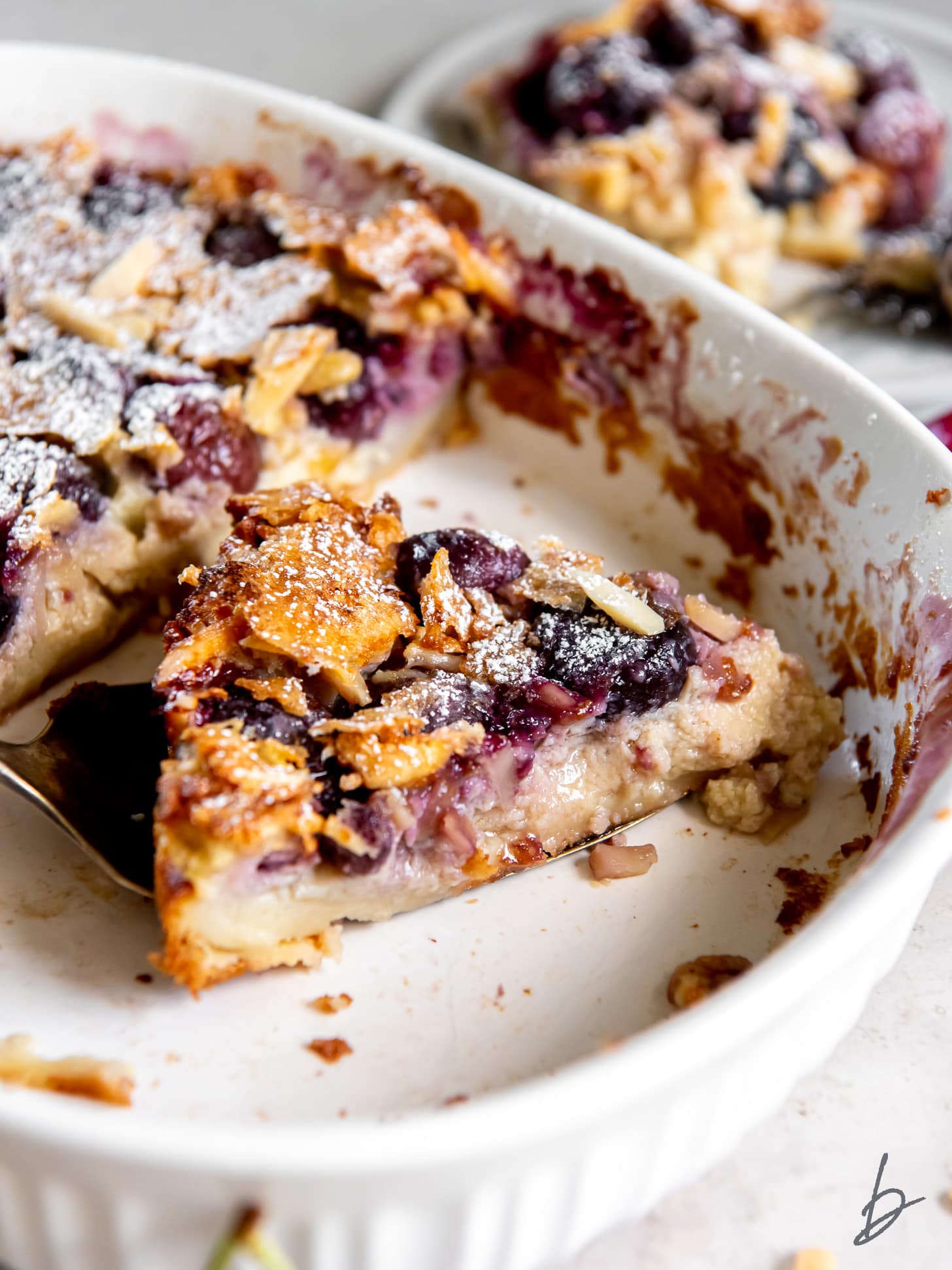 slice of cherry clafoutis with almonds in a baking dish.