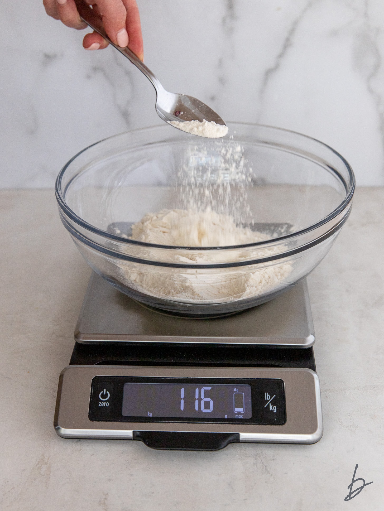 spoon sprinkling flour into a bowl on a kitchen scale.