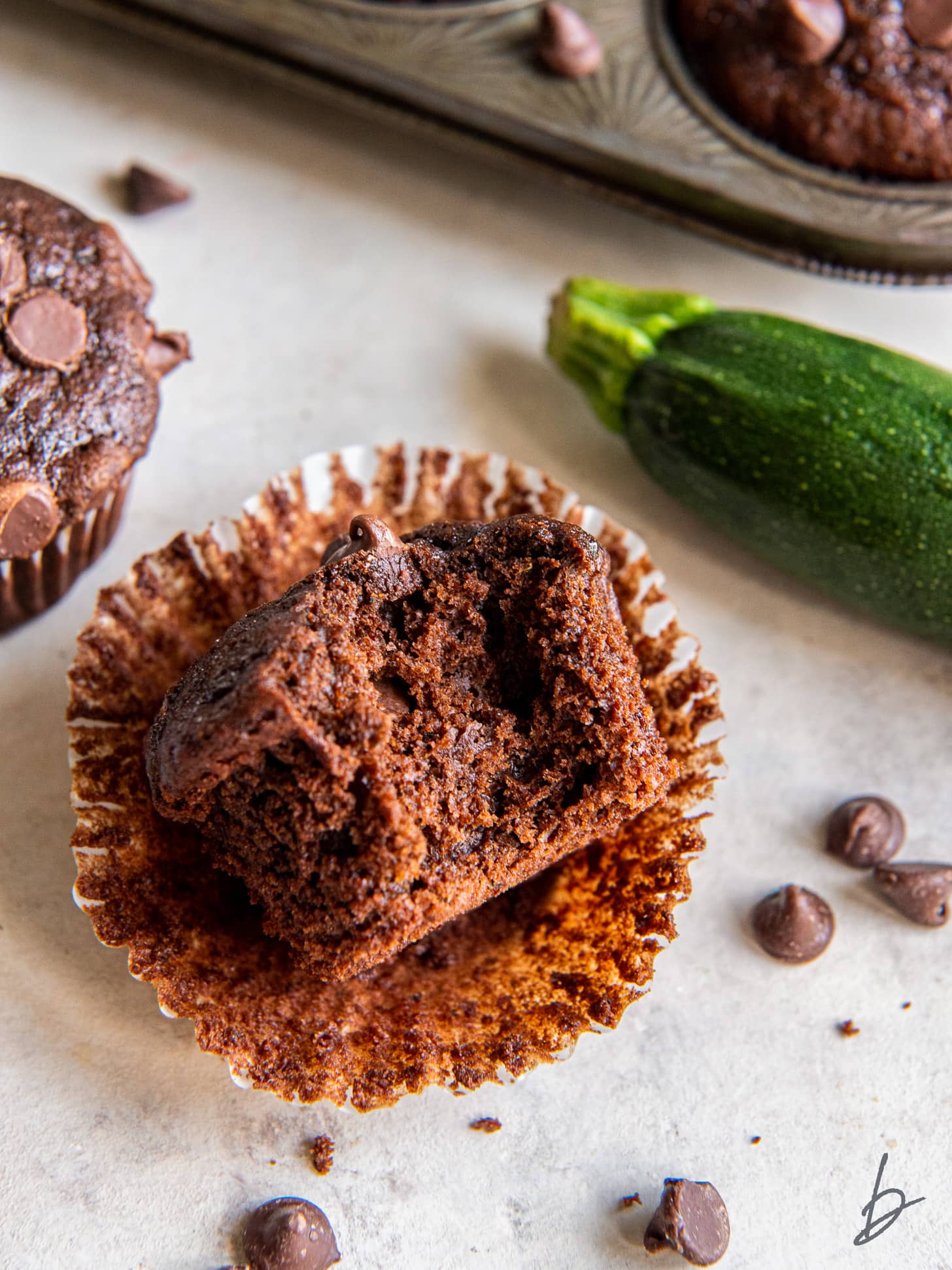 chocolate zucchini muffin with a bite sitting on open paper liner.