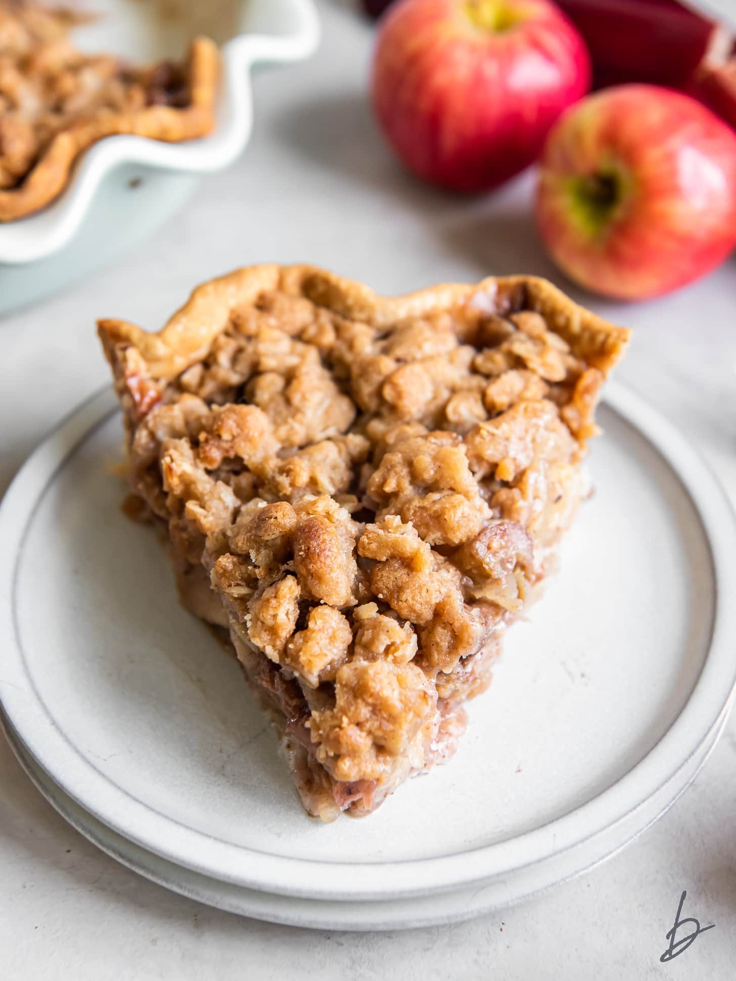 slice of apple rhubarb pie with crumb topping on a plate.