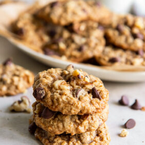 stack of three walnut oatmeal cookies in front of a plate of more cookies.