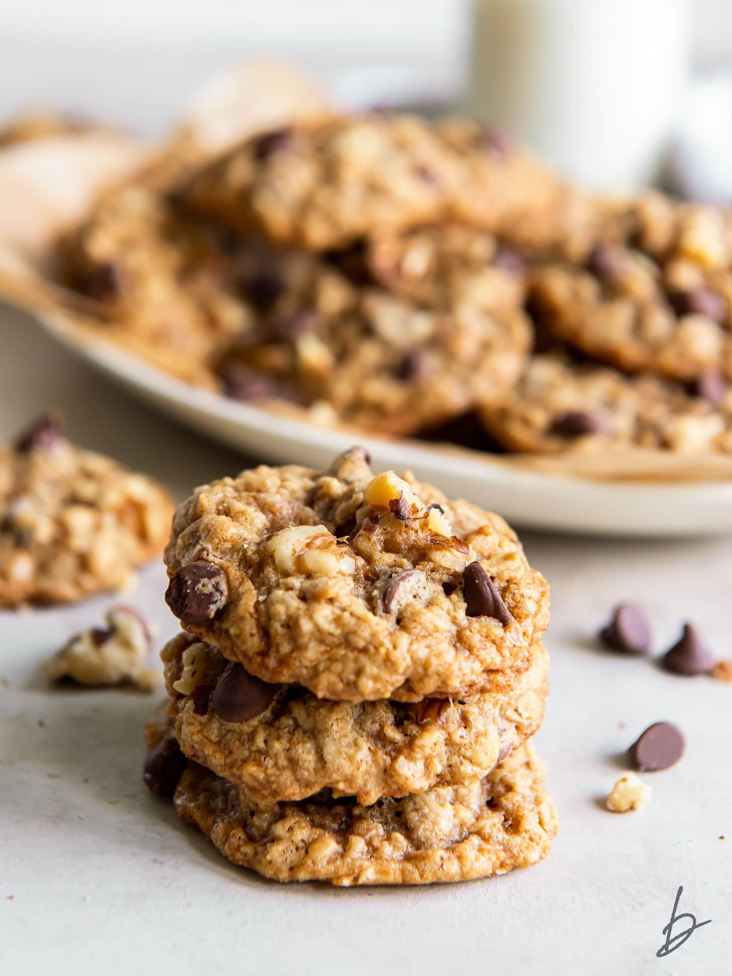 stack of three walnut oatmeal cookies in front of a plate of more cookies.