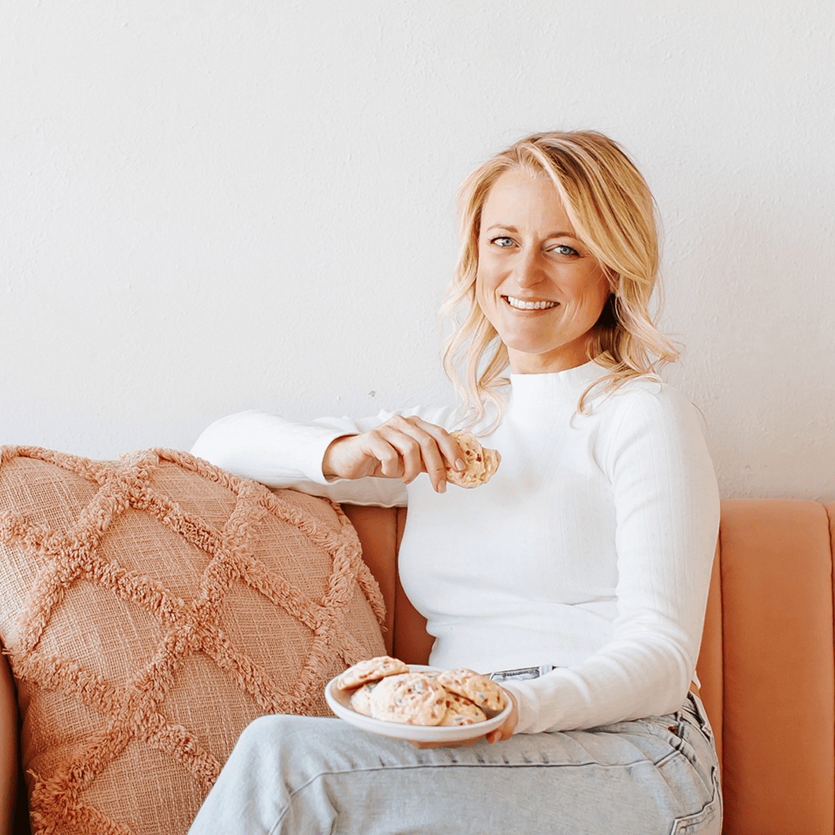 haley williams, blonde woman, holding a cookie and sitting on couch.